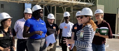 Students tour a company site while wearing safety helmets.